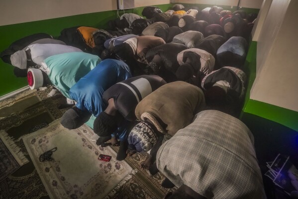 Imam Omar Niass, third from left top, lead evening prayers for African migrants, before the breaking of Ramadan fast and the serving of a festive meal called an iftar, Friday March 15, 2024, at Bronx's Masjid Ansaru-Deen mosque in New York. (AP Photo/Bebeto Matthews)